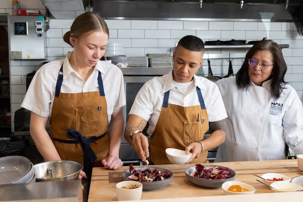 Two HRM students and their professor plating food in the kitchen