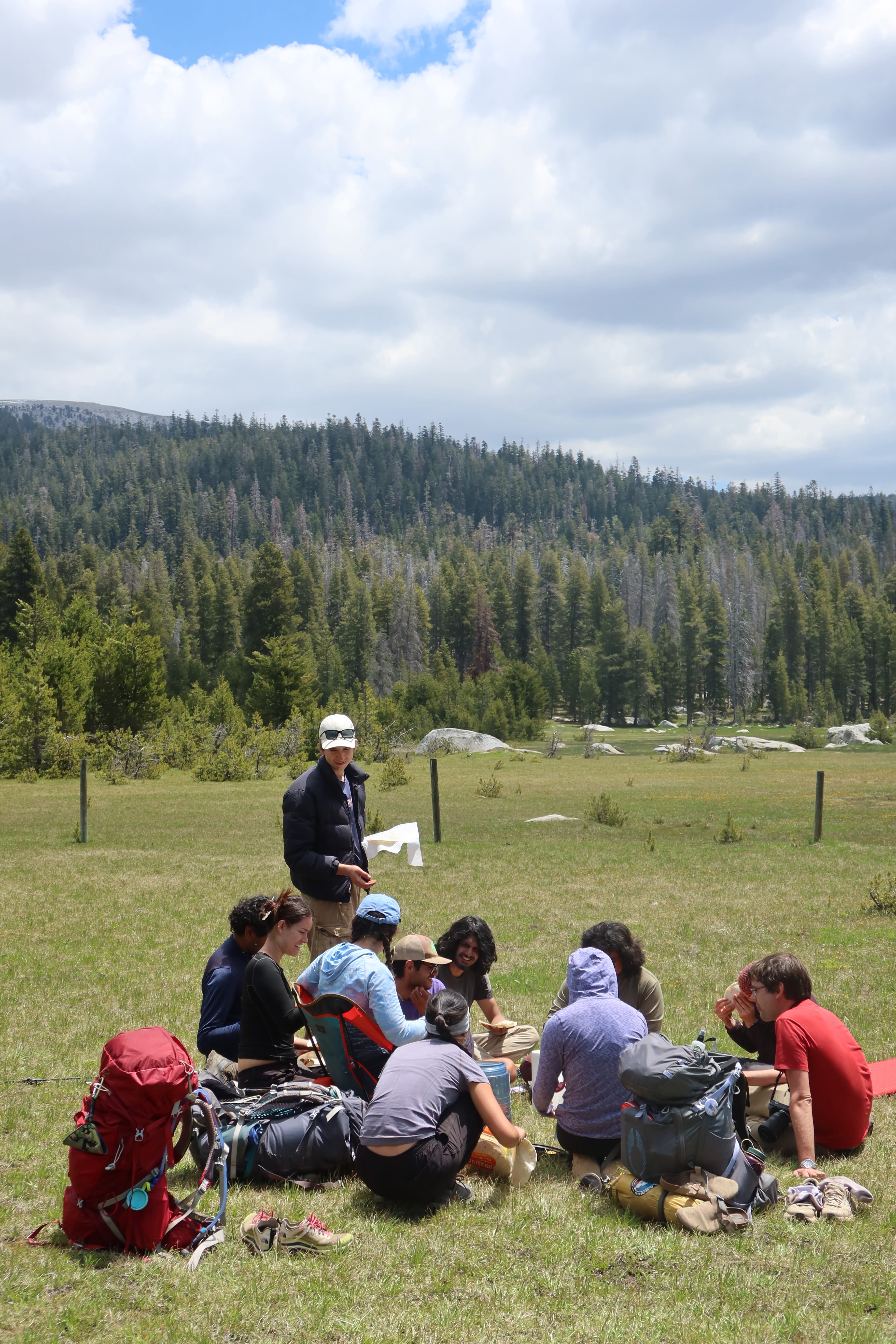 Students sit together in a meadow eating lunch.