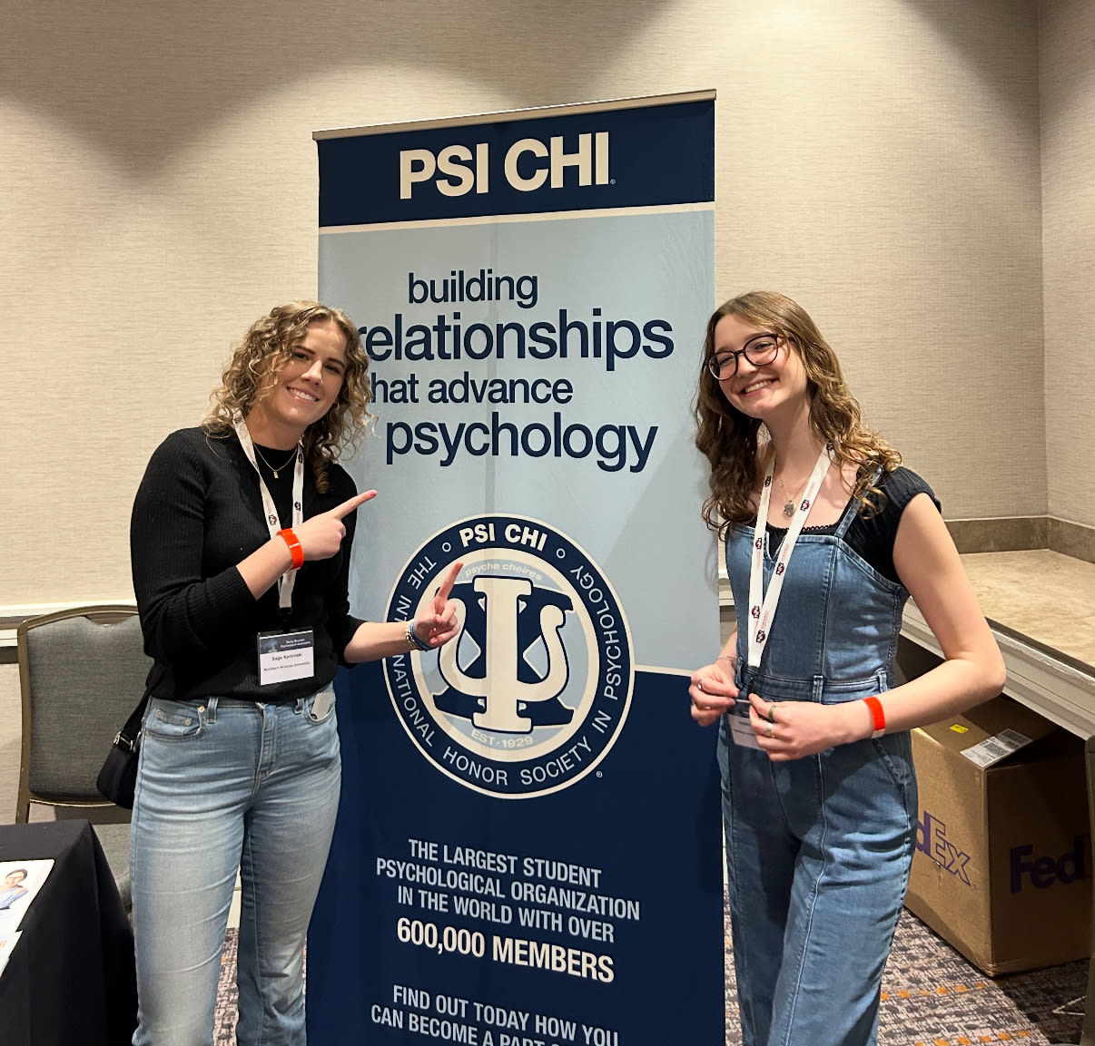 Two NAU Psychology Club members posing in front of a banner for Psi Chi