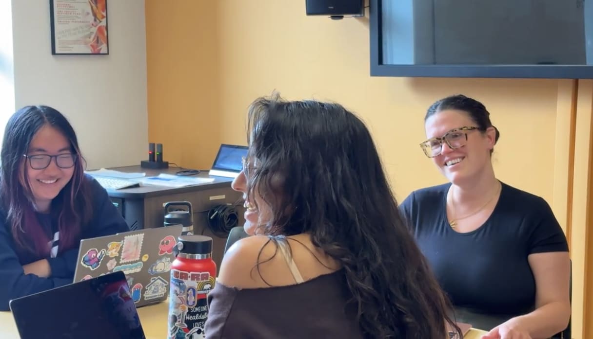 Three students around a table, talking and smiling