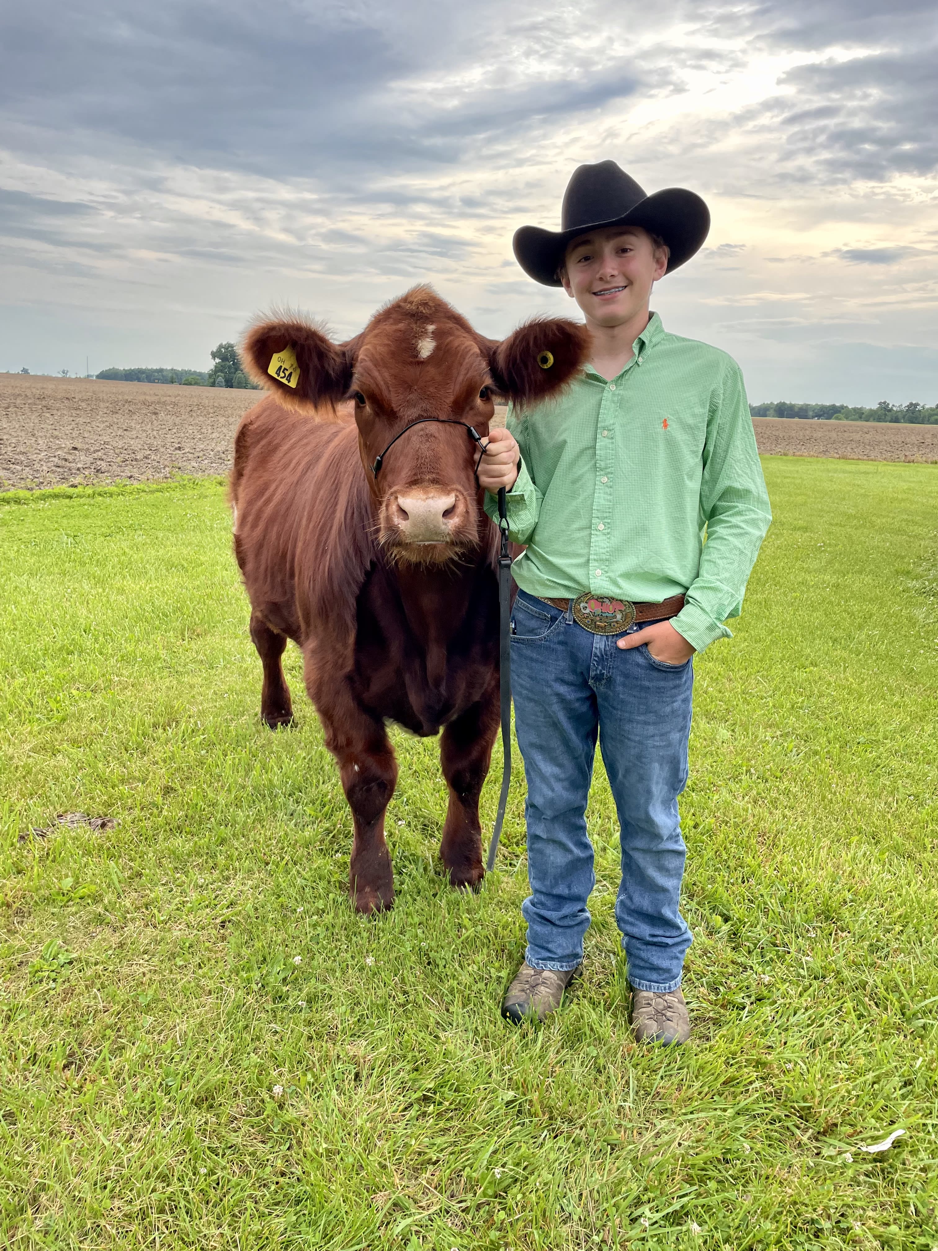 A young boy in a light green button up stands to the right of a steer. He holds it close with a rope
