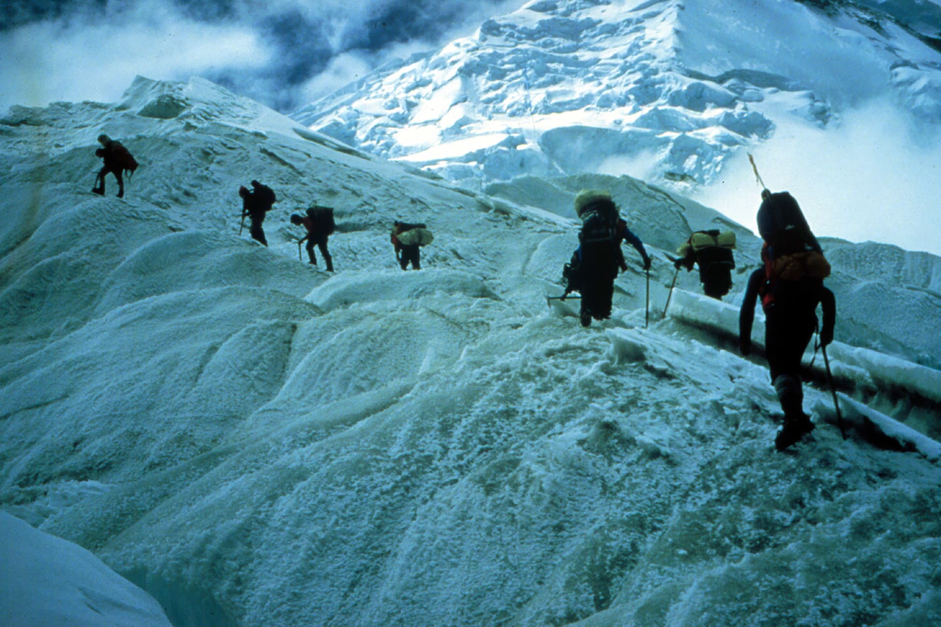 Researchers traverse near a snowy mountain range's edge
