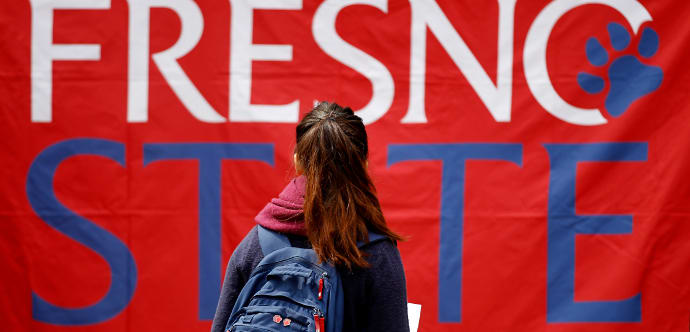 A Fresno State female student gazes at a large banner with the Fresno State logo