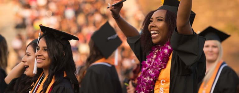 Student with hands in the air wearing a graduation cap and gown