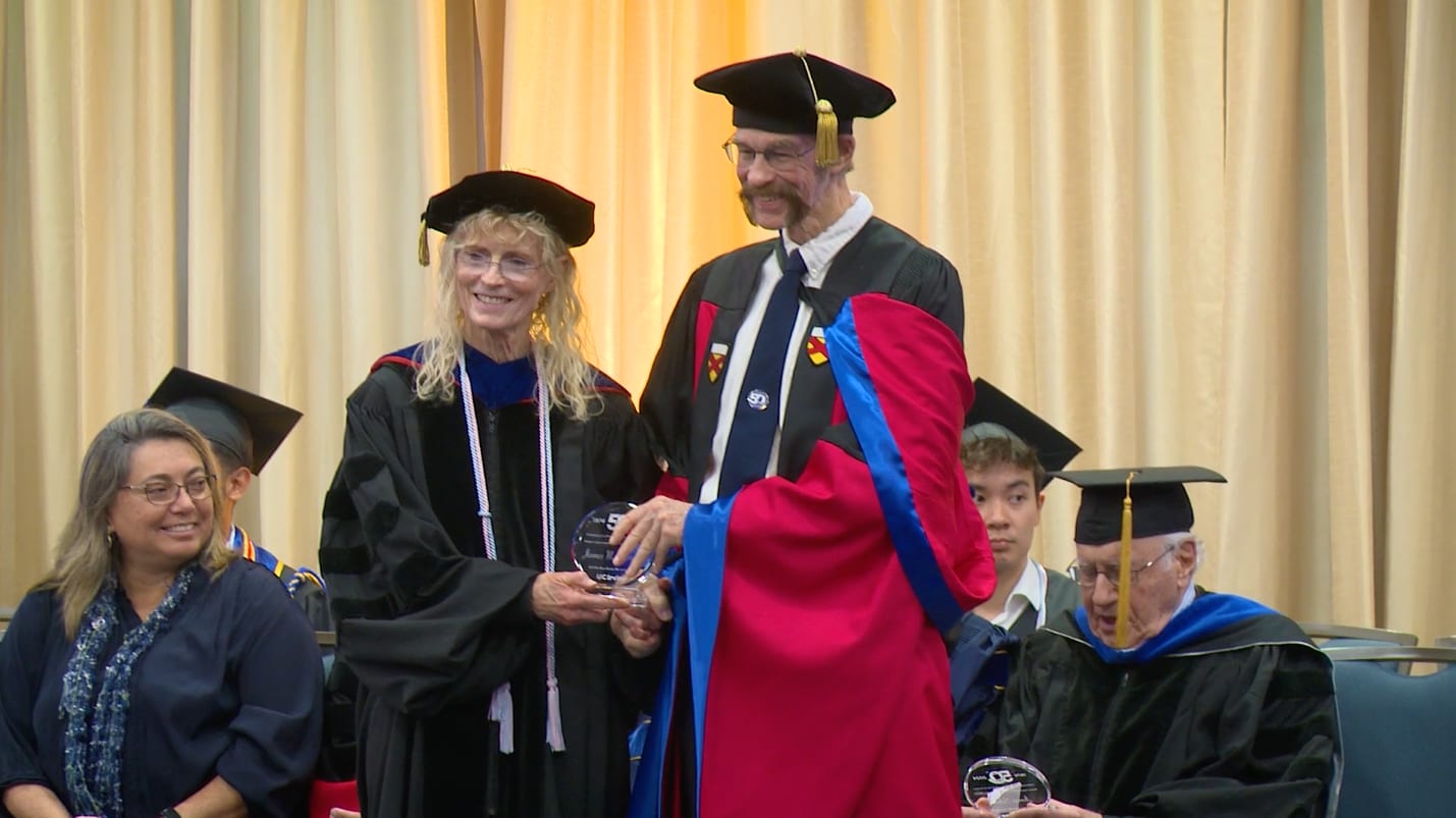 A PBK member in cap and red graduation gown receiving an award from a PBK board member in cap and black graduation gown.