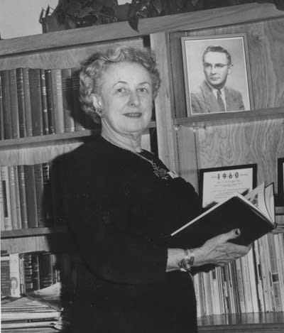 Dean Mary A. Maher holding a book in her office in front of a bookshelf