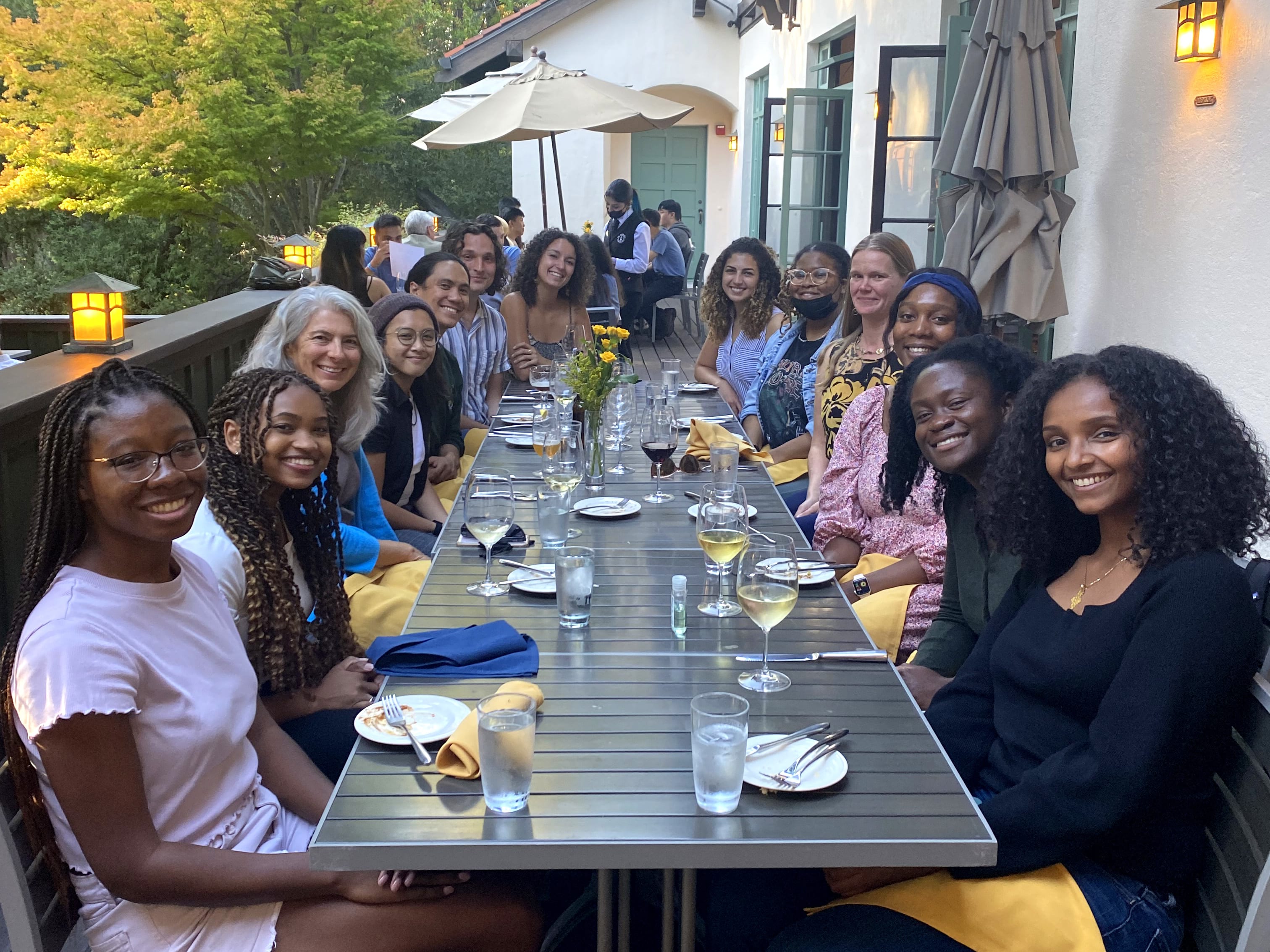 Diverse group of students, faculty, and staff at an outdoor dinner table smiling for a photo