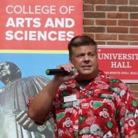 Scott Gale standing before a 'College of Arts and Sciences' poster and University Hall