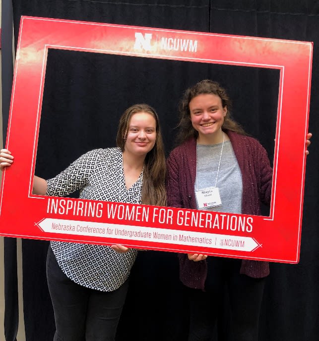 A couple of women holding a red sign

Description automatically generated