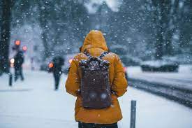 An individual wearing a yellow snow coat and a grey backpack trudges through the snowy environment