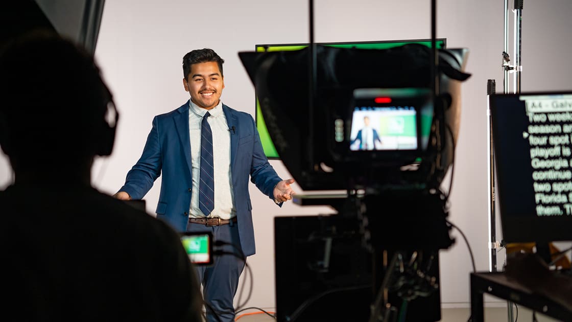 an SOJC student broadcaster stands in front of a video camera