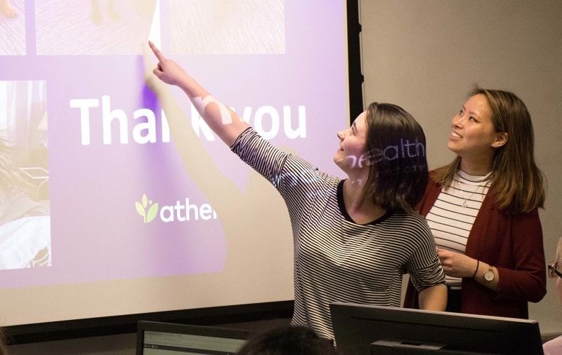 Two PWTC alumni point to a slide as they talk to PWTC students about information design in healthcare.