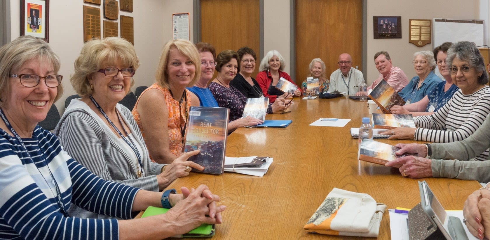 15 people sitting around a table holding books for OLLI's book club.