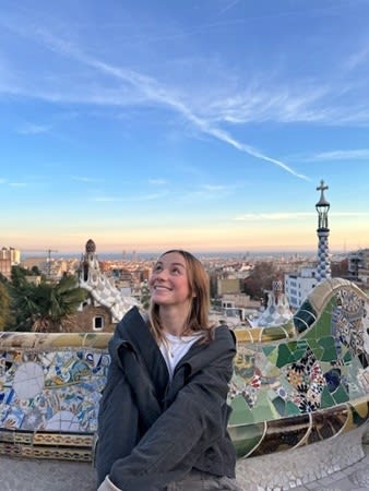 UC Irvine student, Eileen, looks up hopefully from a tiled bench in Park Güell with the Barcelona cityscape behind her.