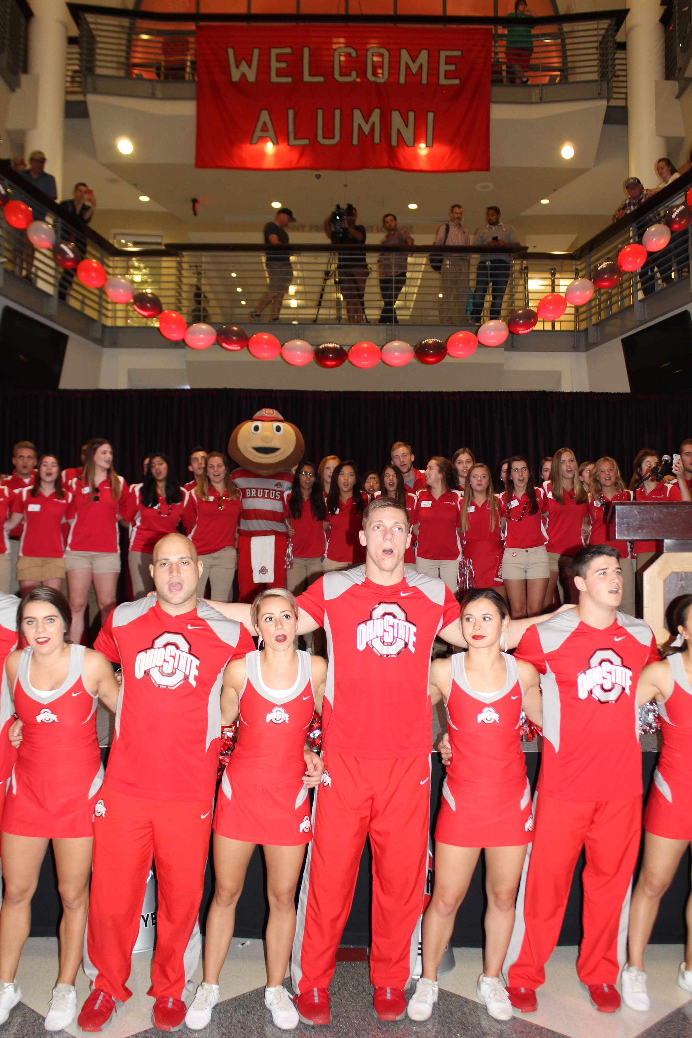 Council members stand on a stage behind OSU cheerleaders. They are welcoming back alums in the Ohio Union