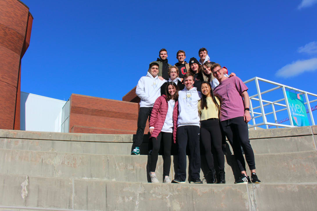 Eleven fraternity members stand on the concrete steps outside Wexner Center for the Arts 
