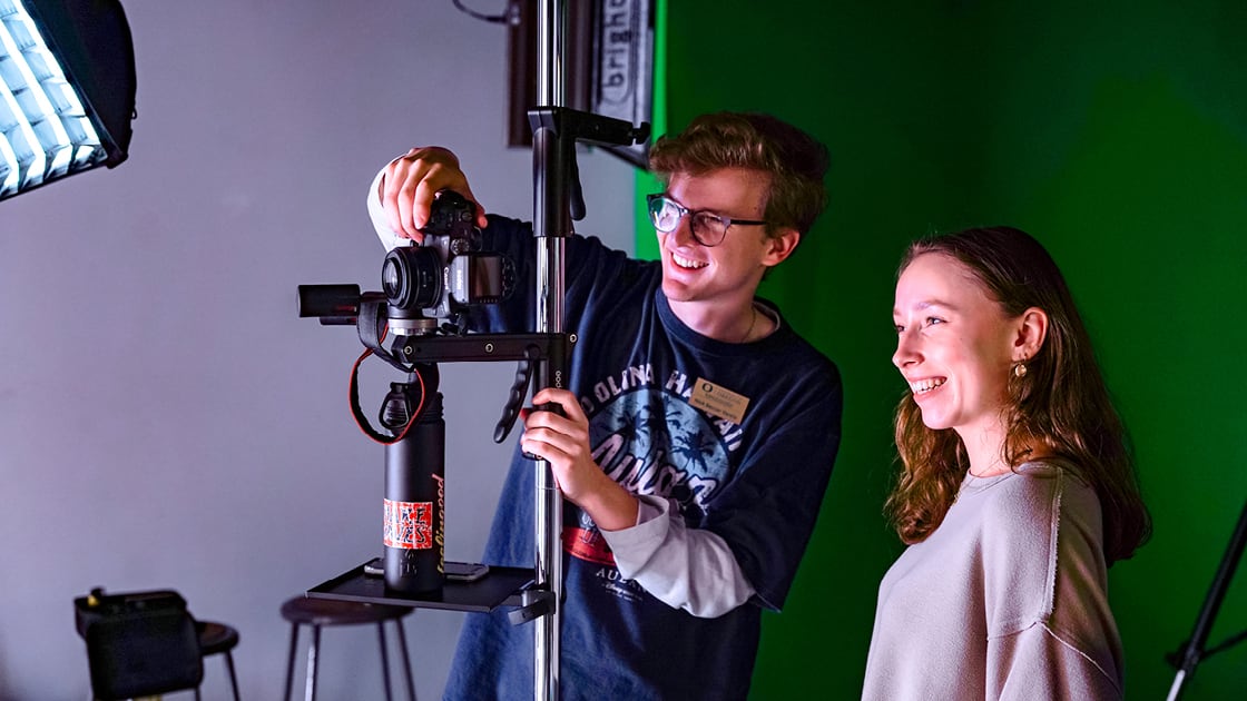 two students adjust camera equipment in the SOJC production studio