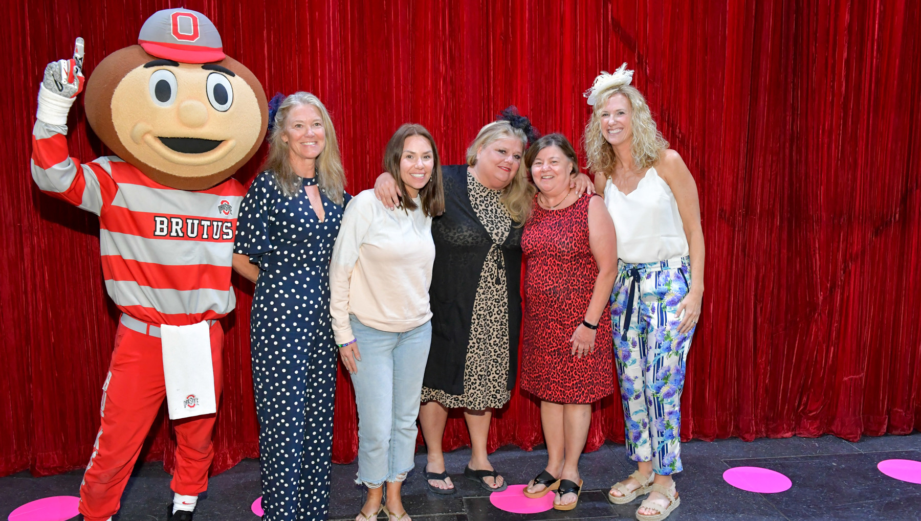 Five individuals stand with Brutus against a red tinsel background