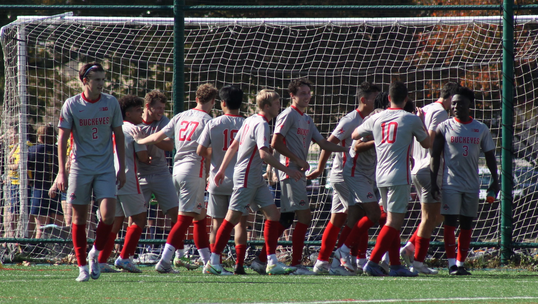 Part of the Men's soccer club in the soccer goal. They are dressed in grey uniforms with red socks