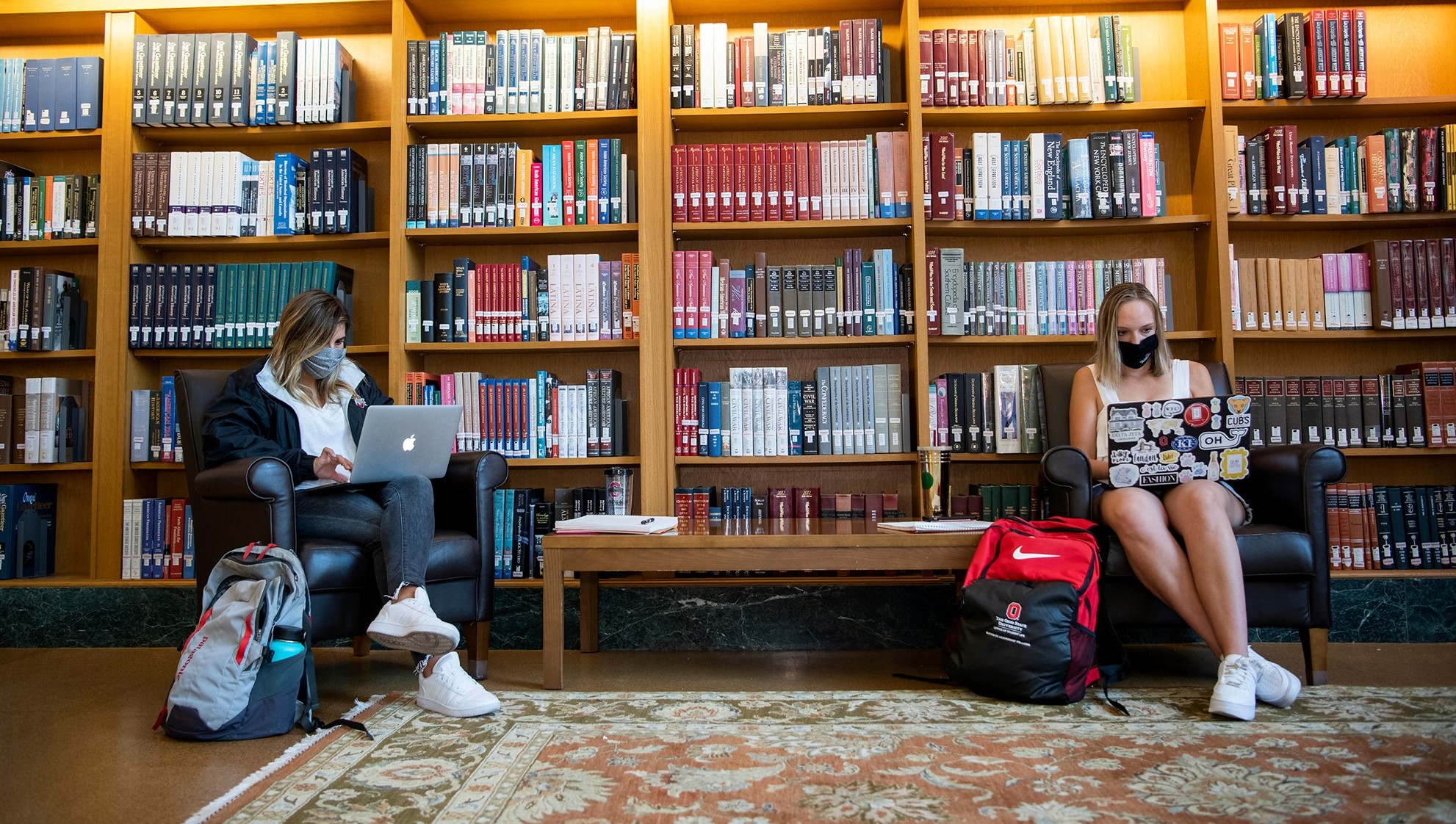 Two students wearing masks studying in library six feet apart