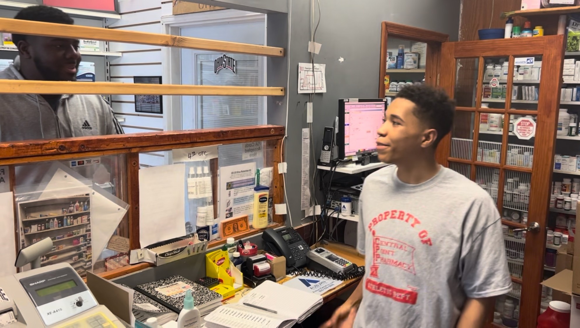 Young man behind the counter at pharmacy speaking to customer across a divider