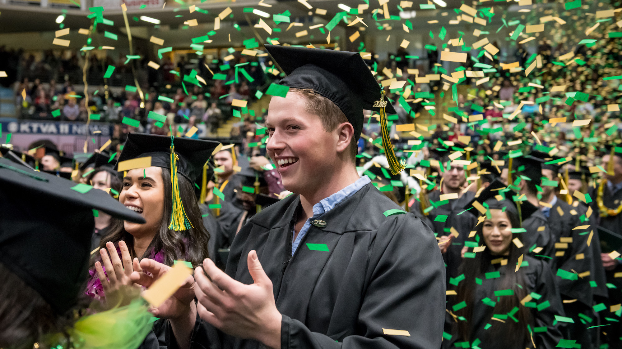 UAA student at graduation, green and gold confetti falling down around him