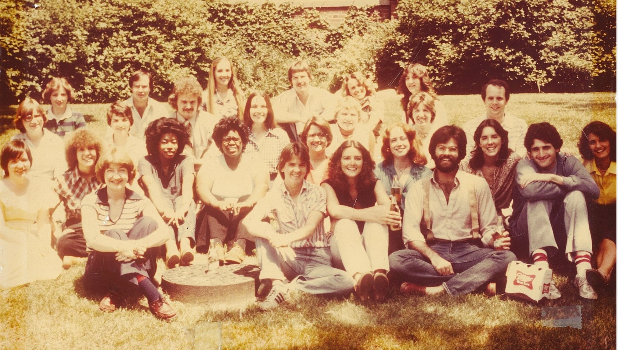 Individuals from the class of 1977 sitting outside on the grass smiling