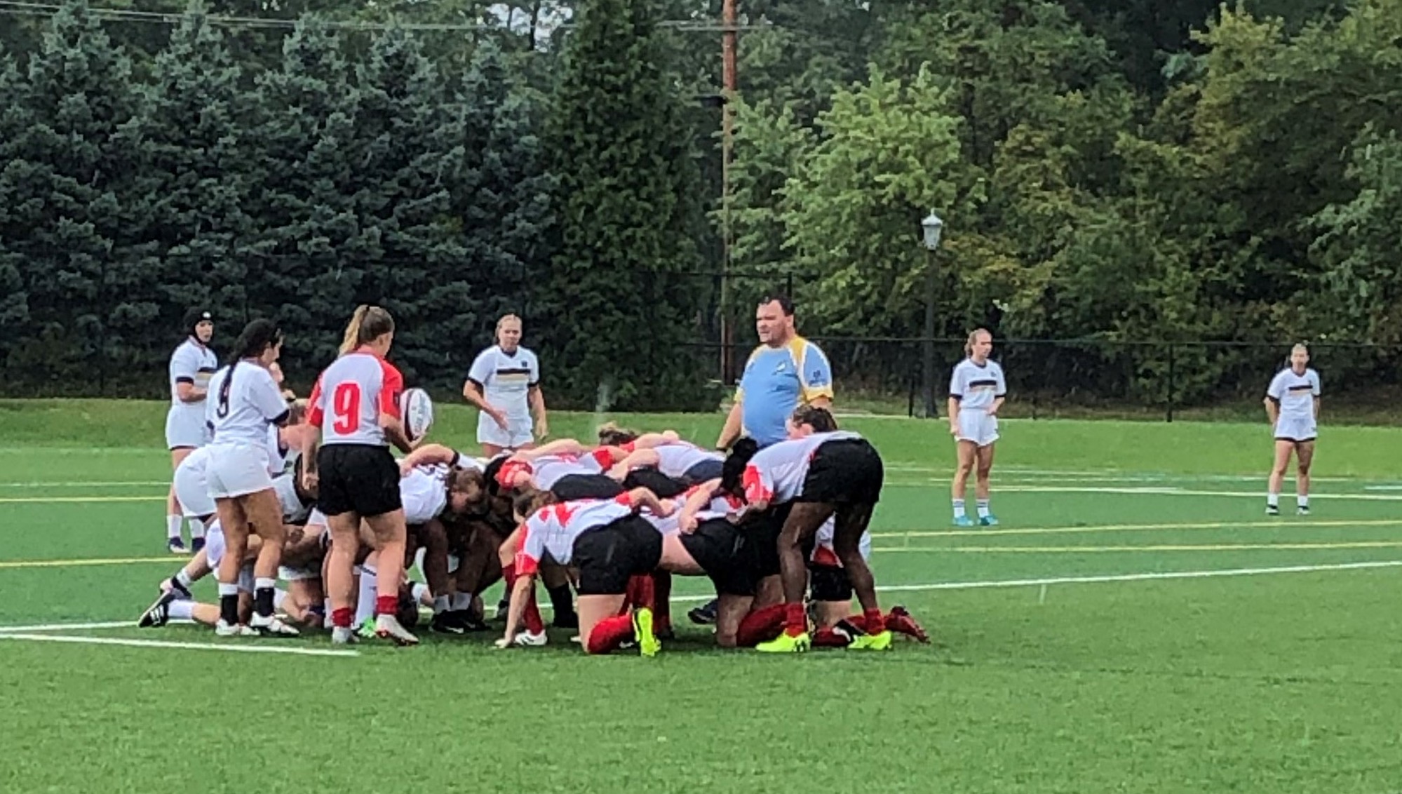 The Women's Club Rugby team huddled tightly with another team on field