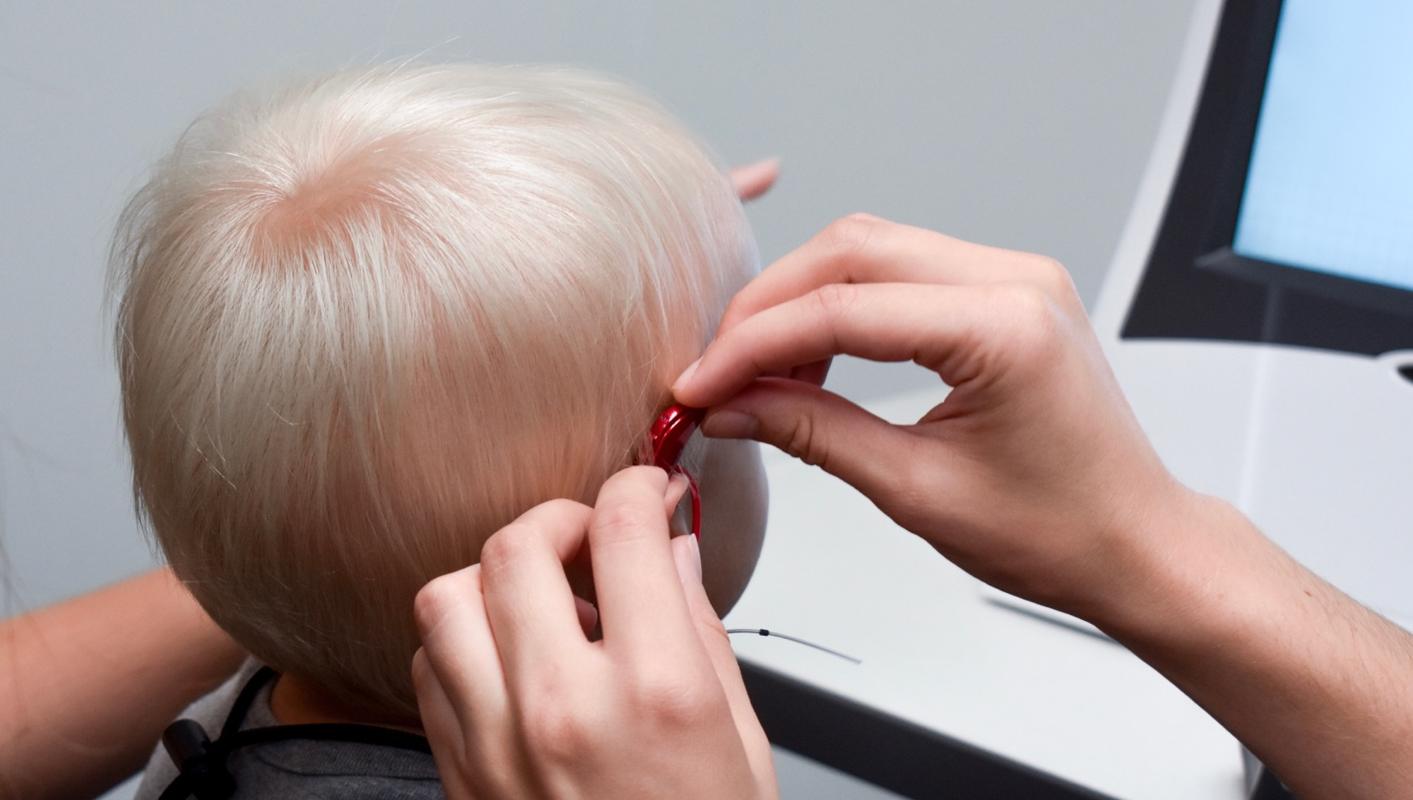 The nurse fits the red hearing aid onto the child's right ear