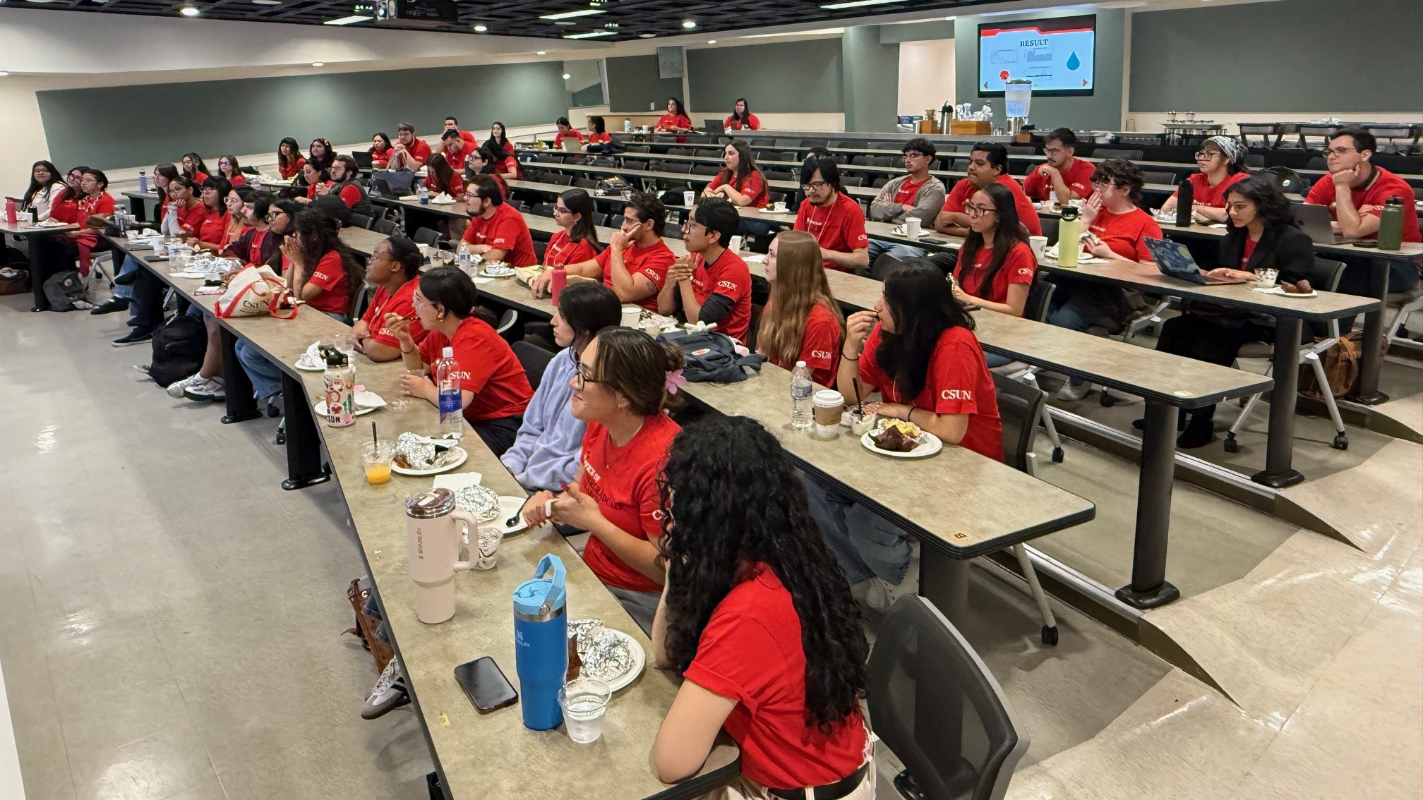 Students wearing red shirts sitting at desks in a lecture hall