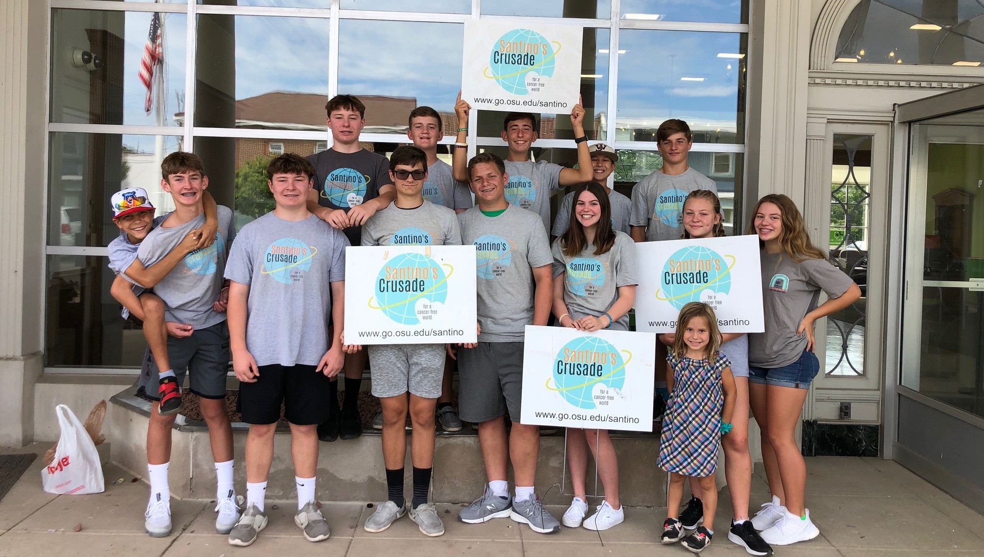 Group of young individuals smiling for a photo while holding Santino's Crusade signs