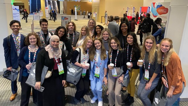 A group of students with white lanyards standing in a lobby of a convention, smiling for a photo