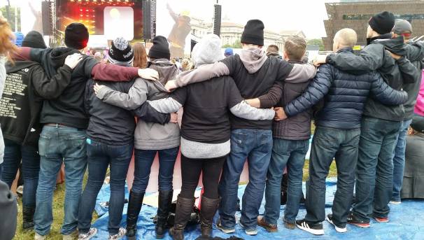 A group of people, all embracing side by side. They face away from the camera