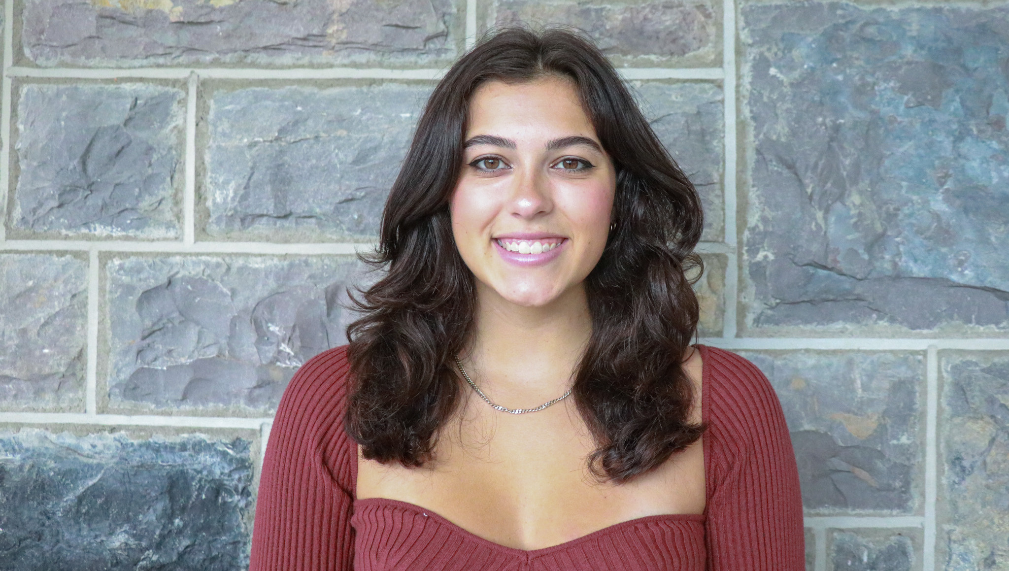 Candidate kayla hess smiles wearing a maroon top in front of a wall of Hokie Stone