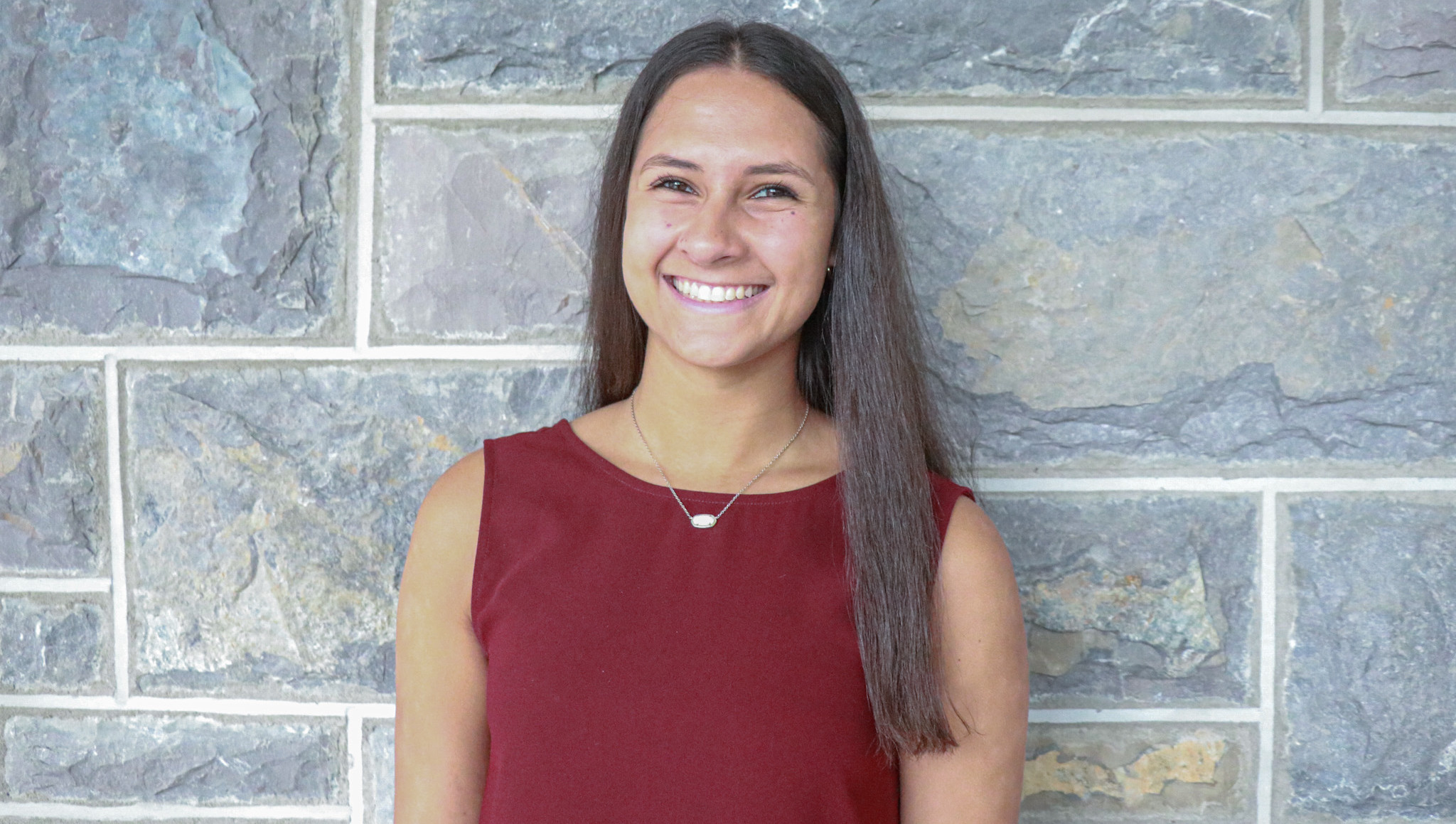 Nicole Bailey, a brunette woman, smiles wearing a maroon top in front of a Hokie Stone background.