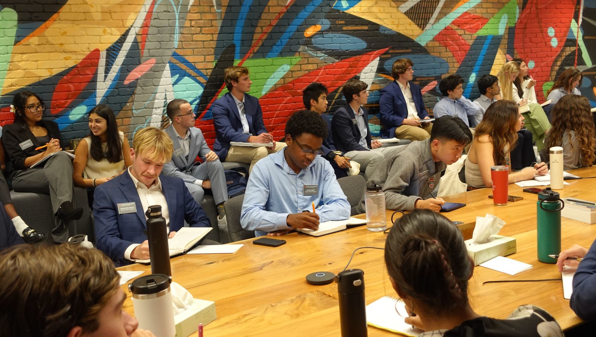 A group of students actively listen and take notes from a guest speaker