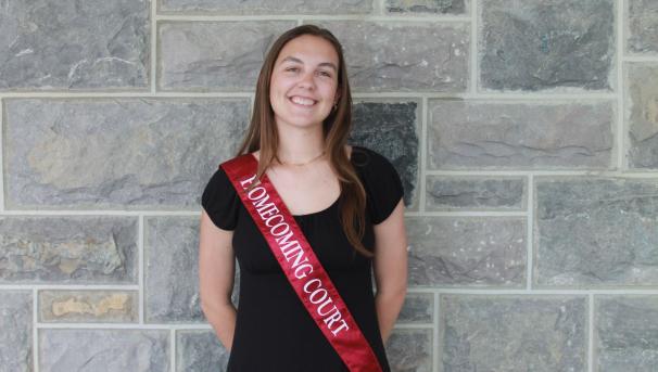 Rachel stands smiling in front of a Hokie Stone wall wearing a maroon Homecoming Court sash