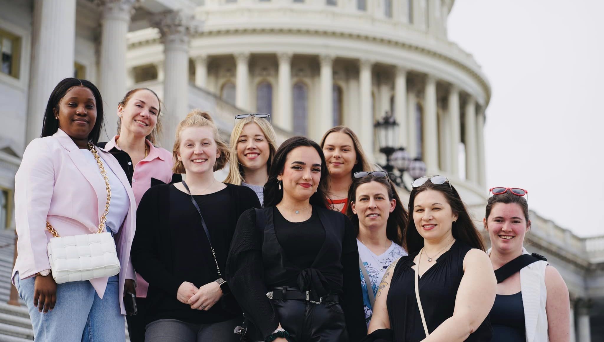 Nine individuals standing outside on steps of a building smiling for a group photo