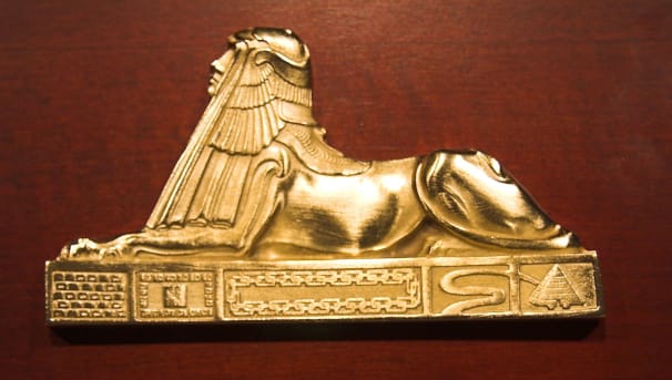 A pin of a sphinx that is plated in gold