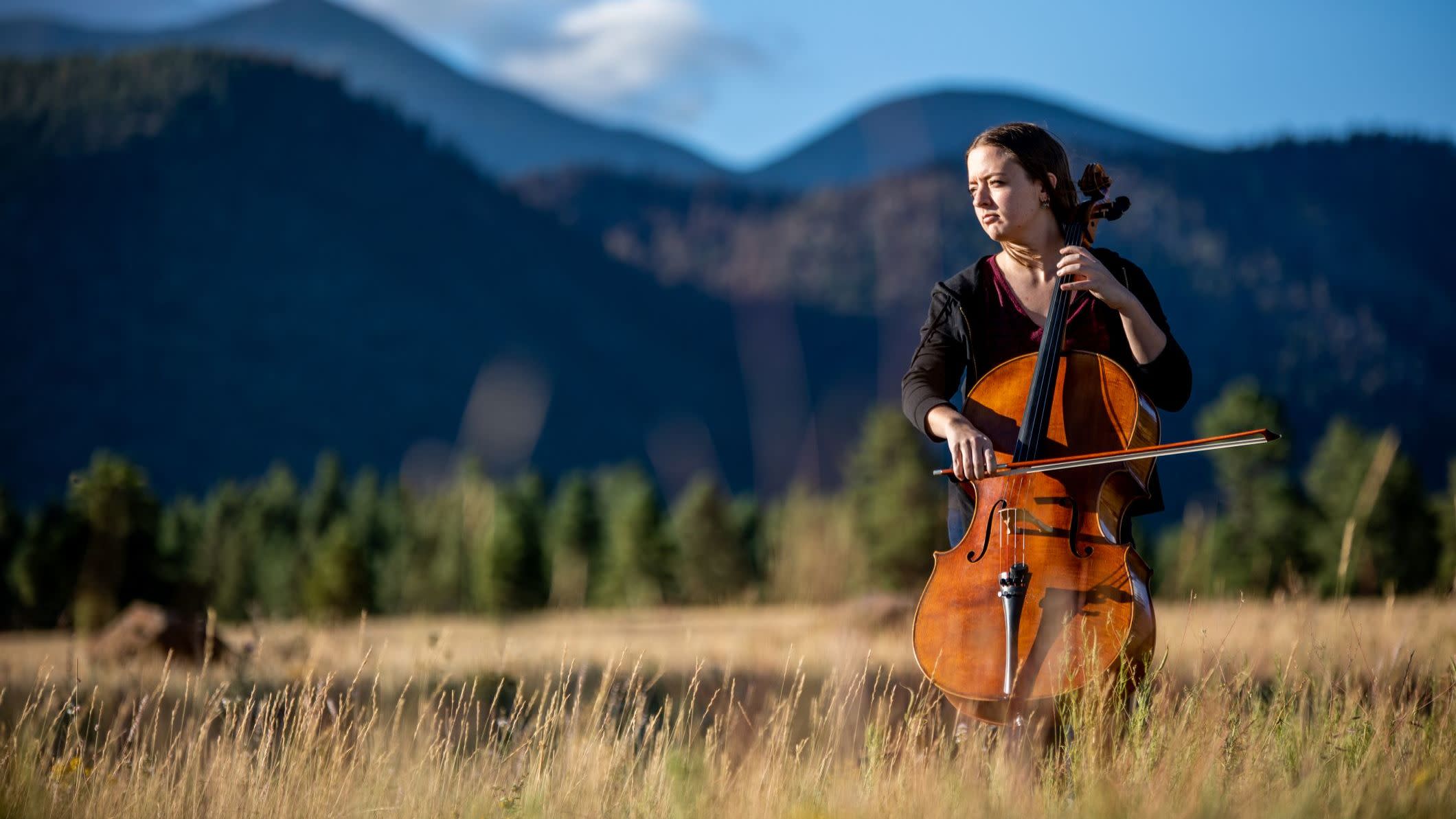 An NAU music student pictured playing the bass outdoors with the peaks in the background.
