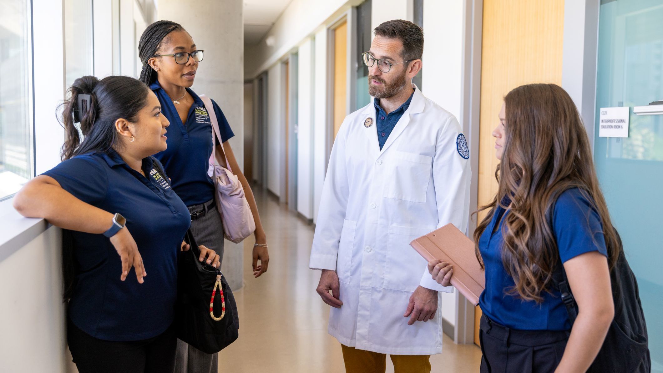 Four CHHS students talk amongst one another in a campus hallway.