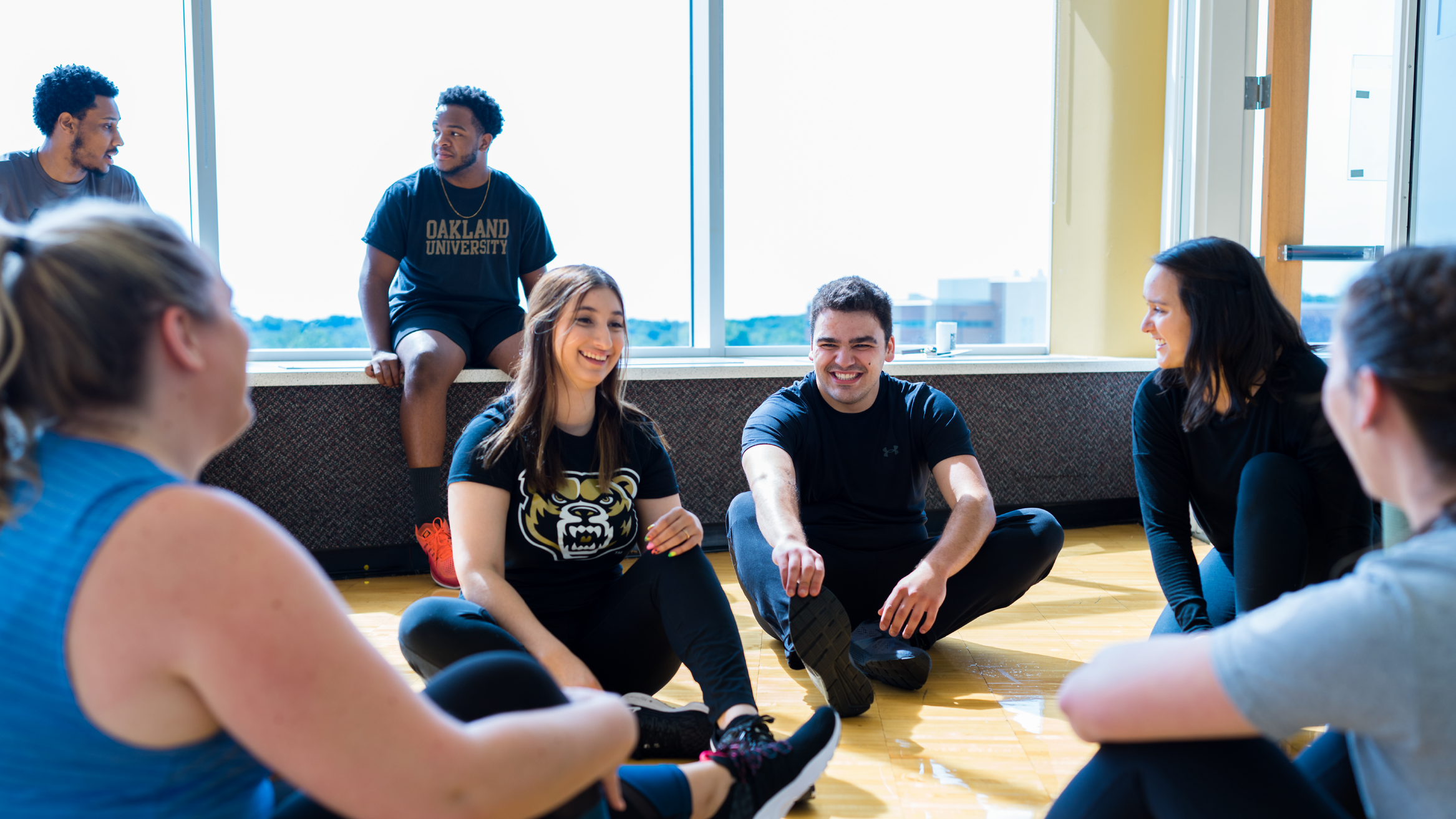 A group of students sits on the floor and stretches together.