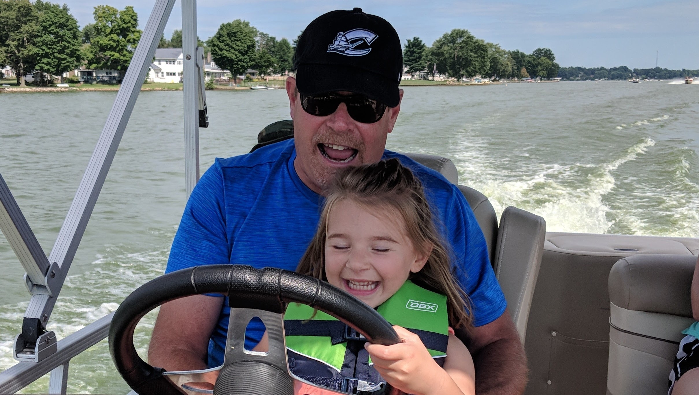 Child sitting on an individual's lap while steering a boat on the lake