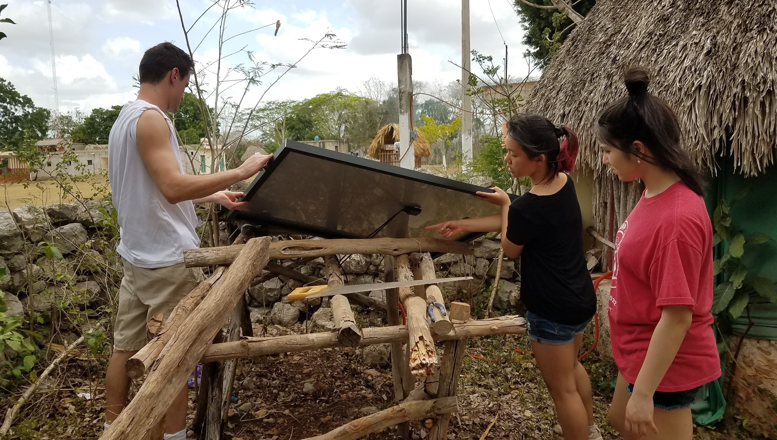 Students installing something outside a thatched hut