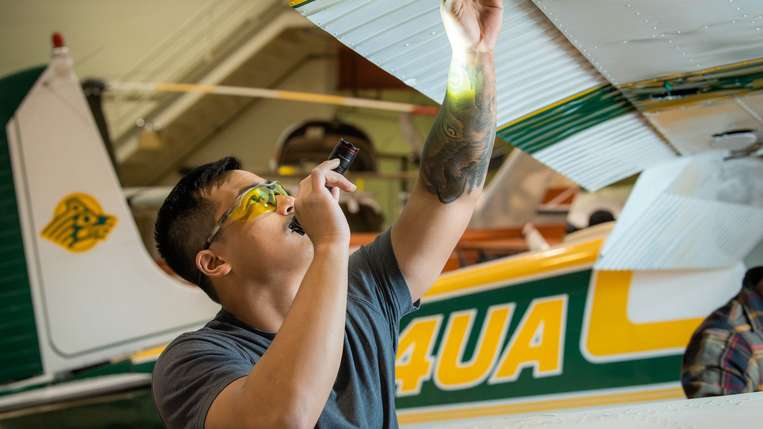 AVIATION MAINTENANCE STUDENT AT CTC, WORKS ON GREEN AND GOLD SEAWOLF PLANE