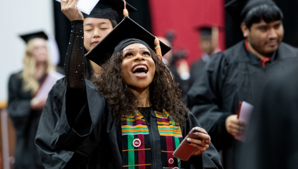 A graduate with a large smile holds her diploma high into the air at