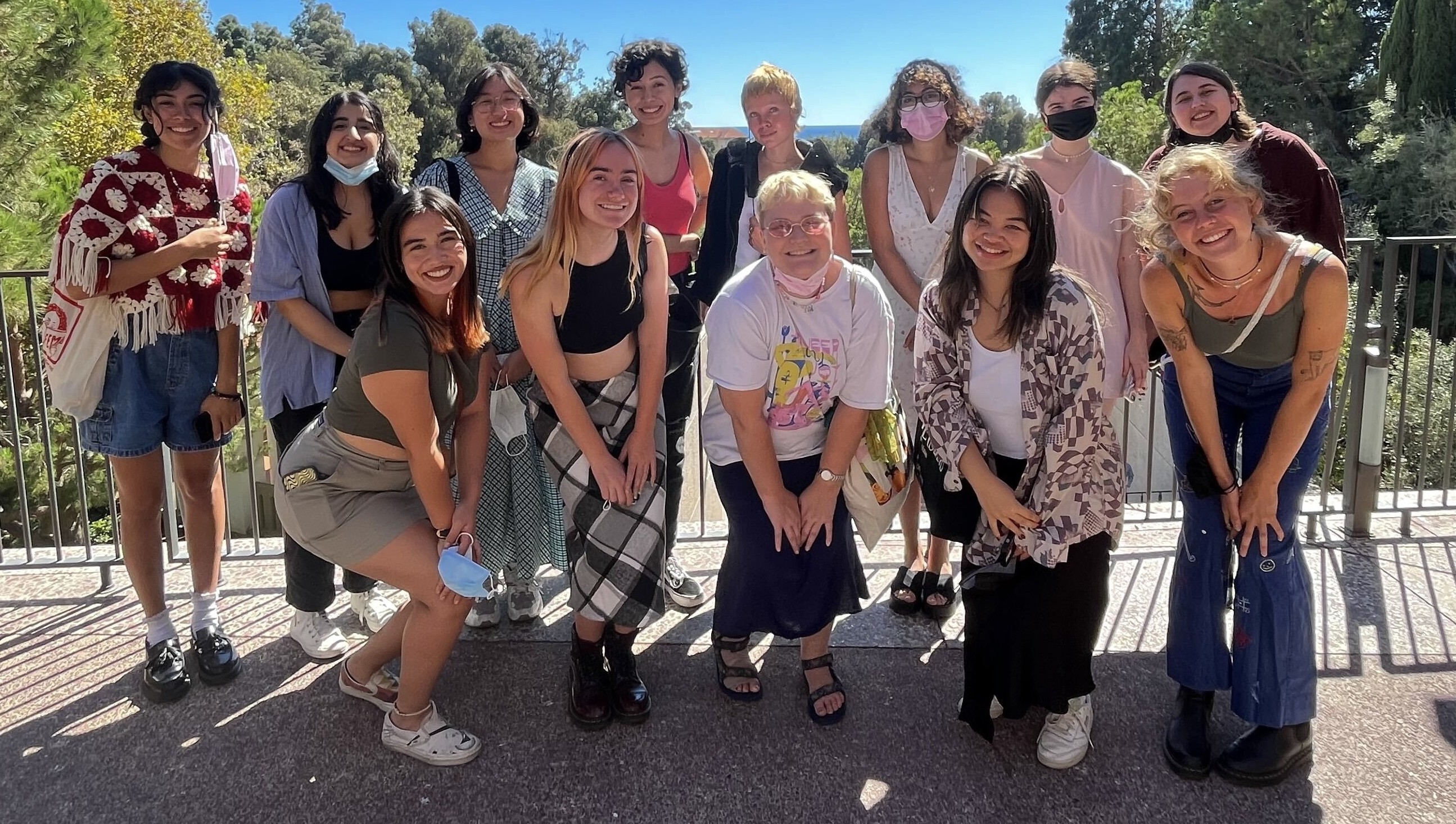 a group of people smiling, standing next to a ledge in front of a view of trees and the ocean