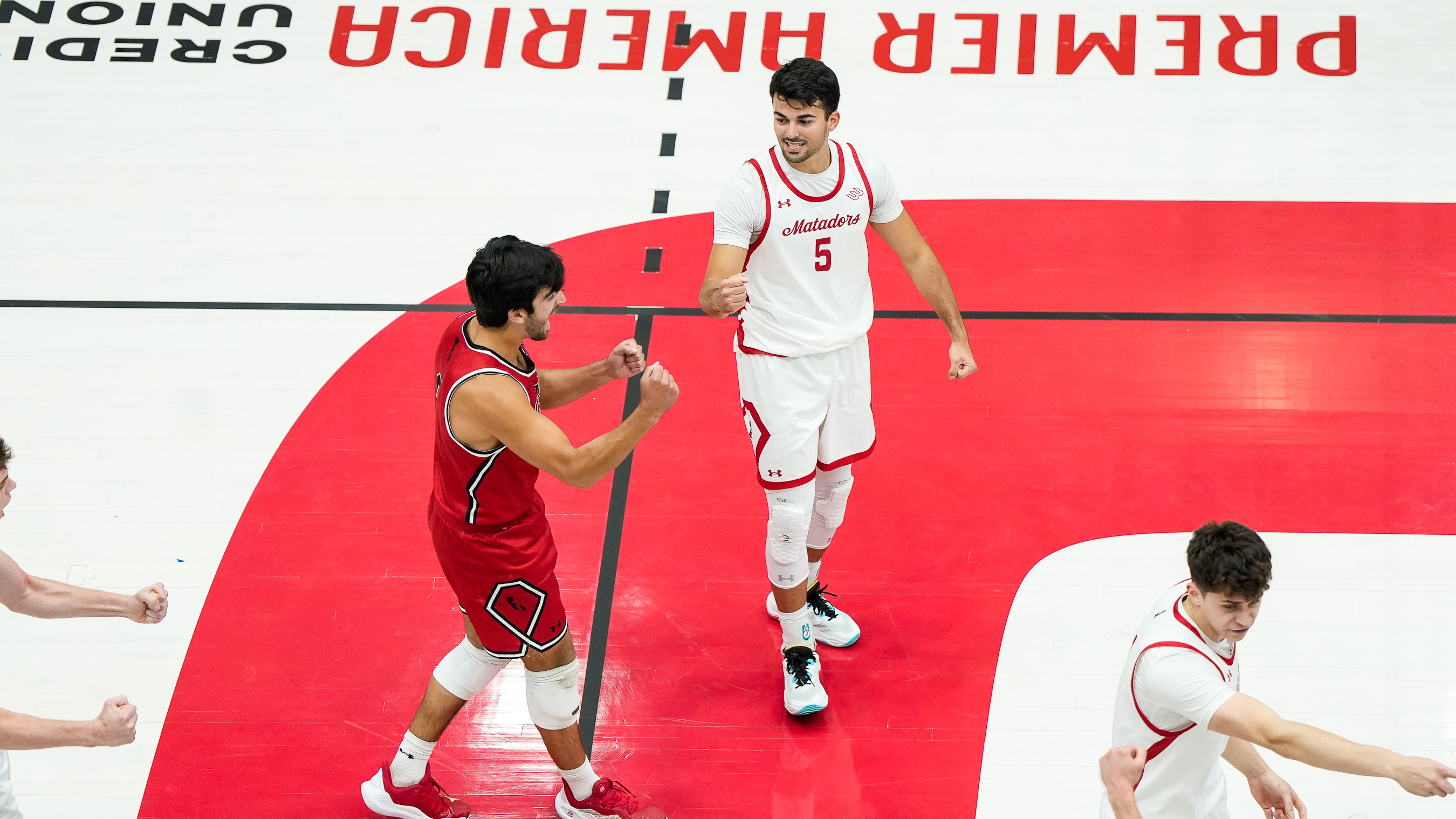 Two volleyball players on a red court celebrate with clenched fists during a match.