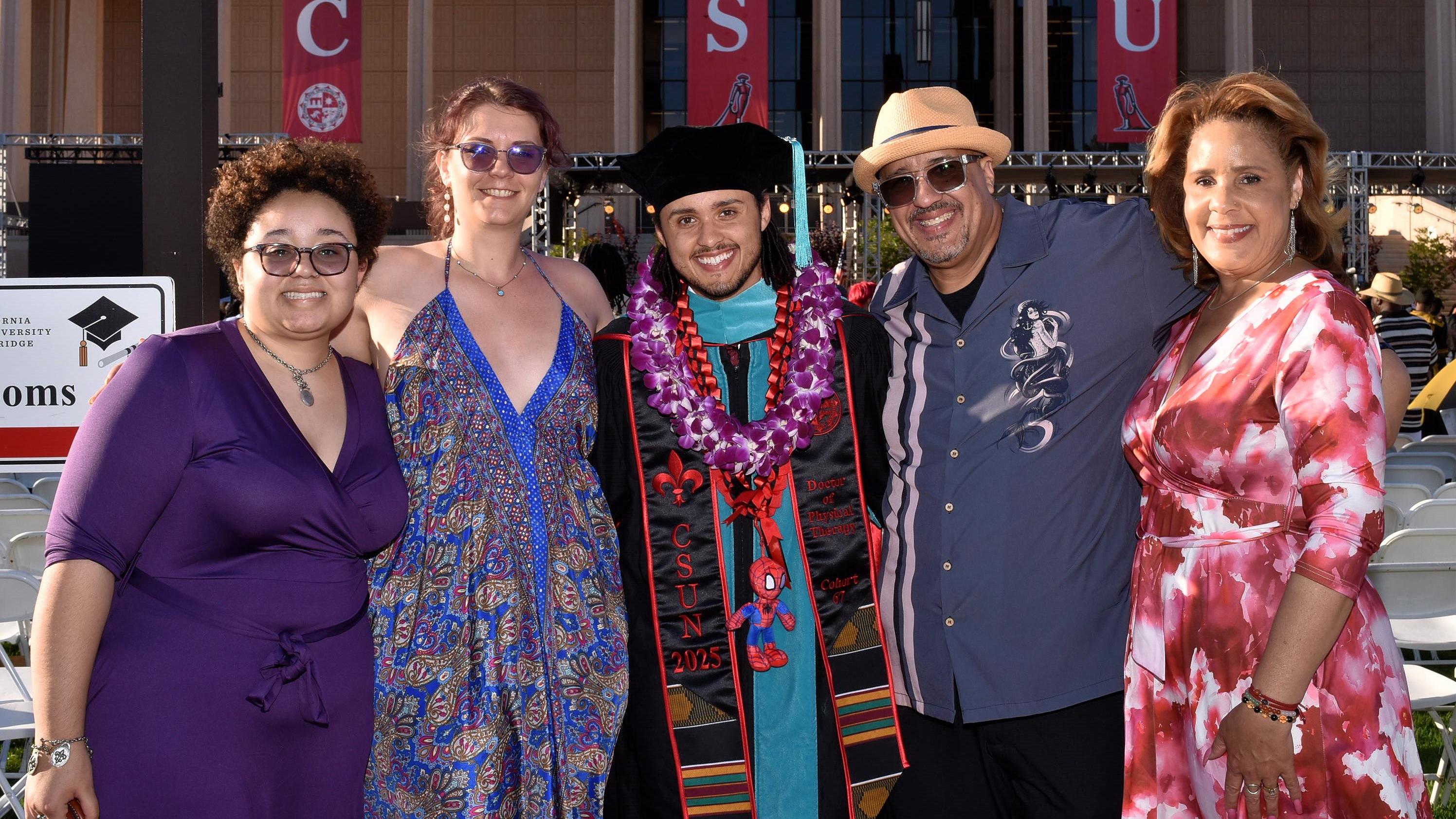 Student posing in graduation regalia with family
