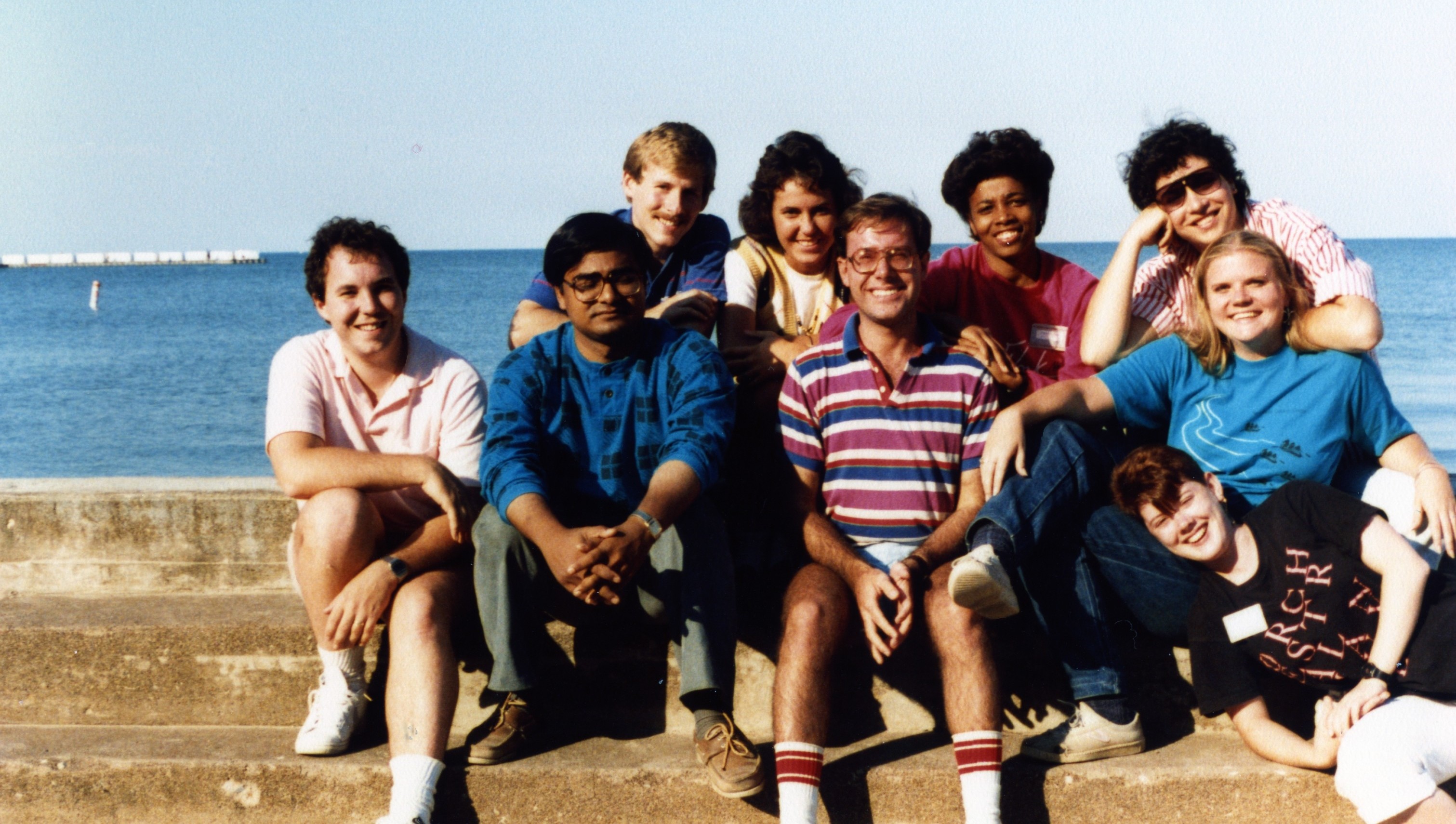 Group of individuals from the 1986 Cohort sitting on steps outside smiling for a photo